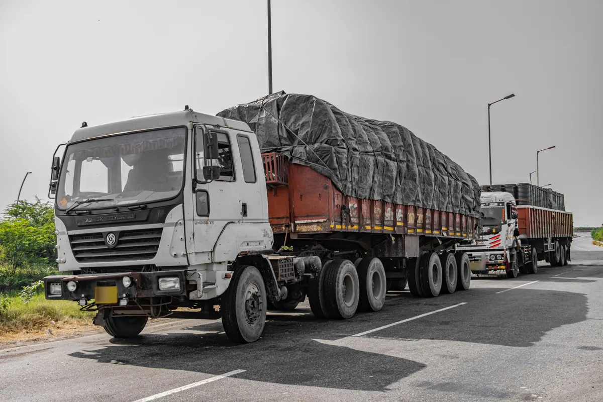 Heavy cargo trucks with tarpaulin-covered loads lined up along a highway shoulder